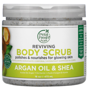 A woman's hand holding a jar of Petal Fresh Argan Oil & Shea Reviving Body Scrub, with the product name and branding visible on the label.