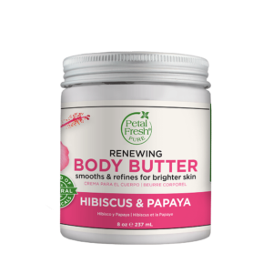 Image of Petal Fresh Renewing Hibiscus Papaya Body Butter. The jar is open, revealing a rich, creamy body butter inside, with a light pink color and a tropical hibiscus flower on the label. In the background, there are tropical leaves and flowers, highlighting the natural ingredients used in the product.